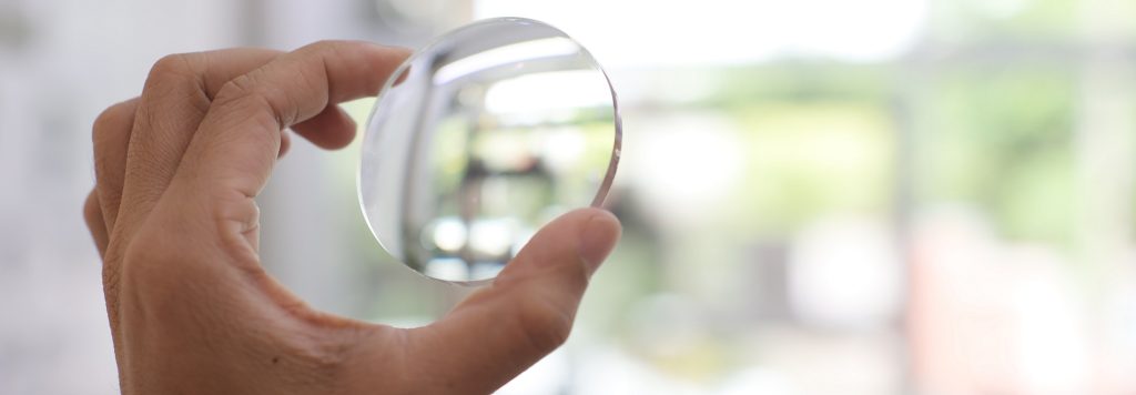 Close up of hand holding lens against the light in an optical lab