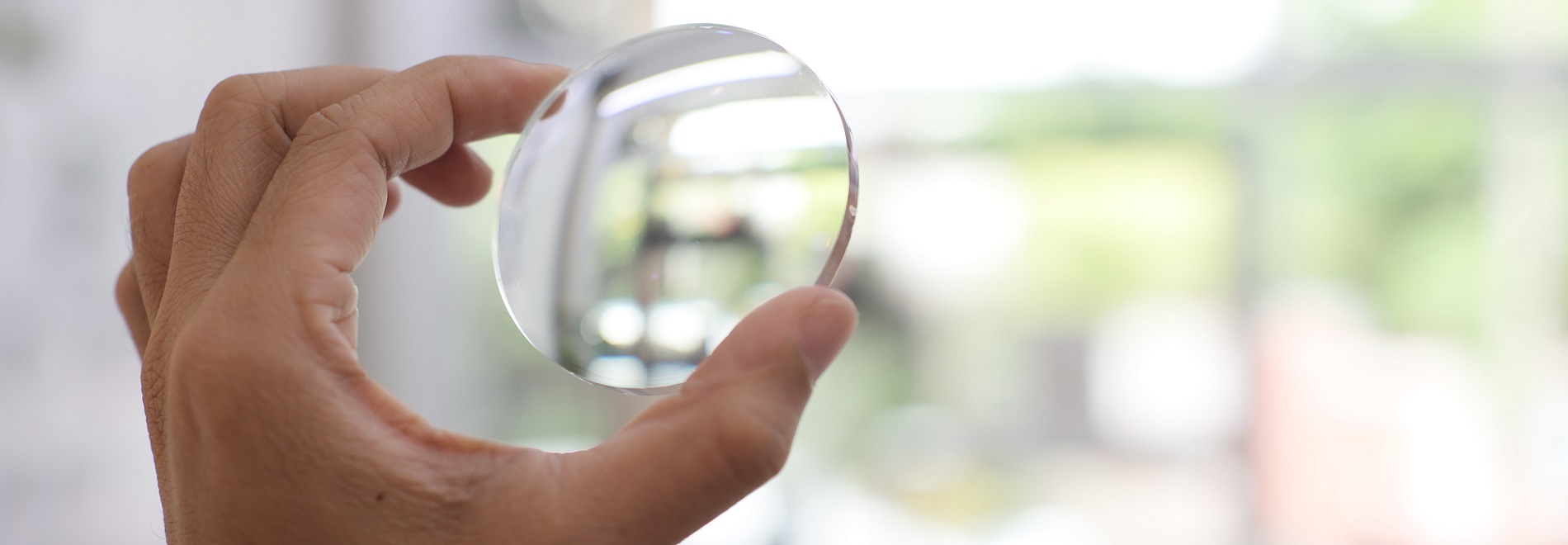 Close up of hand holding lens against the light in an optical lab