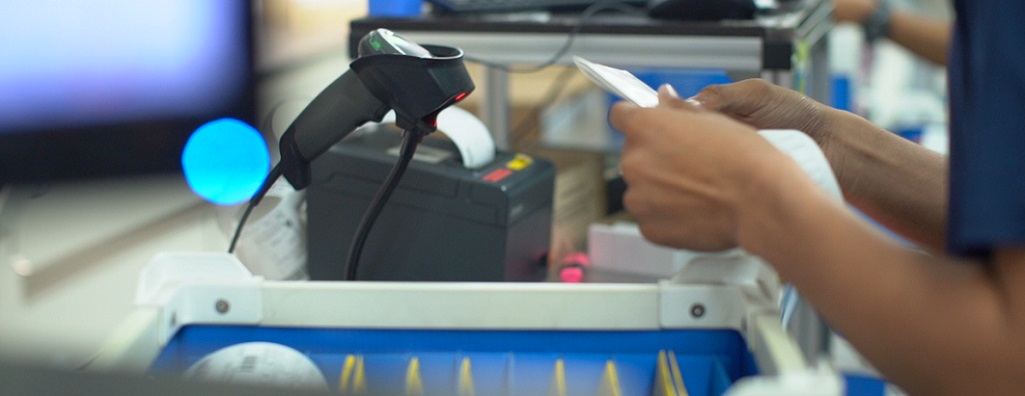 Optical lab technician scanning a job ticket with a barcode reader beside a lab tray, illustrating real-time job tracking and production verification.